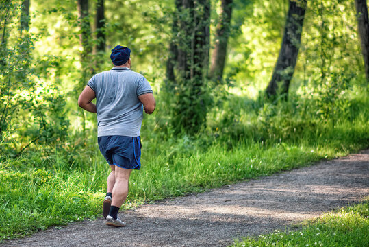 An overweight man running in a park to lose weight on summer morning.