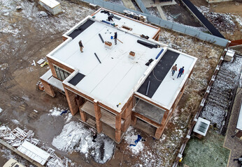 Roofing construction worker installing a flat roof. Bright blue sky in the background.