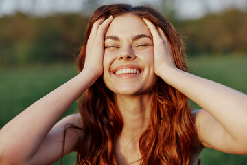 A beautiful woman with long, wavy red hair smiles for the camera in nature illuminated by sunset...