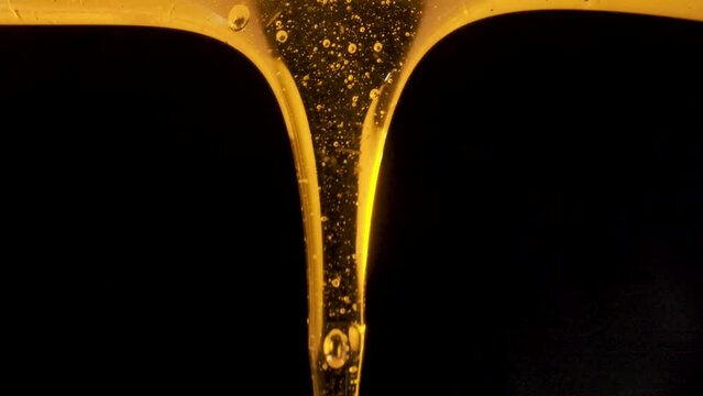 Drops of thick golden honey flowing down on a black background. Close up of sweet nectar or molasses being spilled. Liquid honey pours and drips. Sugar syrup is pouring. Healthy and curative dessert.