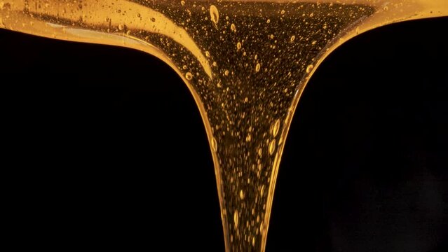 Drops of thick golden honey flowing down on a black background. Close up of sweet nectar or molasses being spilled. Liquid honey pours and drips. Sugar syrup is pouring. Healthy and curative dessert.