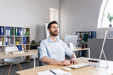 Businessman in the office with closed eyes performs breathing exercises, freelancer working on the...