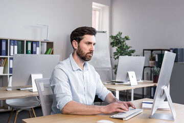 Fototapeta premium Concentrated and pensive businessman working in the office at the computer, paperwork broker, man looking at the monitor