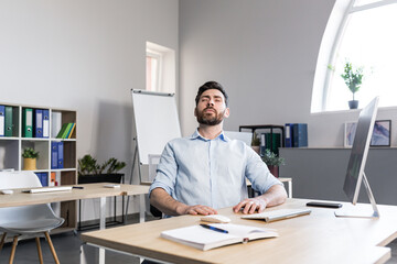 Businessman in the office with closed eyes performs breathing exercises, freelancer working on the...
