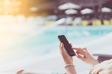 Woman using smartphone and sitting on bed at swimming pool resort abstract background. Technology...