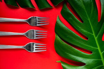 Silver forks and green laeves on red background. Flat-lay. Mockup