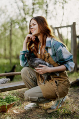 A woman with a smile takes care of the health of a chicken and holds a chicken in her hands while working on a farm in nature feeding the birds organic food