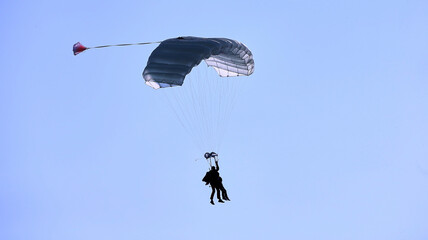 A skydiver with a white parachute canopy against a blue sky and white clouds, close-up.