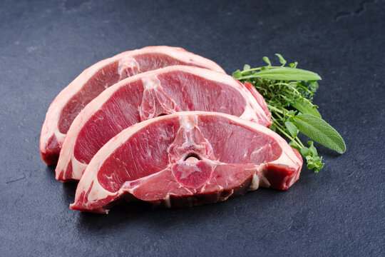 Rohe Lammr&uuml;ckensteaks mit Kr&auml;utern angeboten als close-up auf einem schwarzen Design Board mit Textfreiraum
