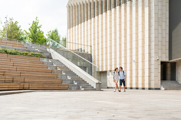Adult students walk near outdoor audience with wooden seats near university campus. Young couple on romantic date. Summer vibes. Education in Europe.