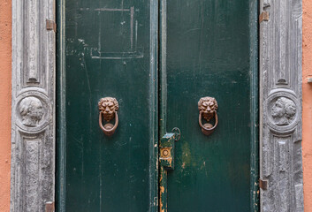 Detail of the entrance door of an old building with door knobs in the shape of lion's heads and a stone frame with bas-reliefs, Genoa, Liguria, Italy