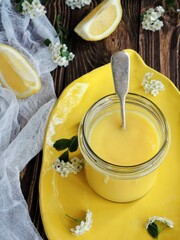 Lemon curd in a glass jar on a brown wooden table with a white flowers