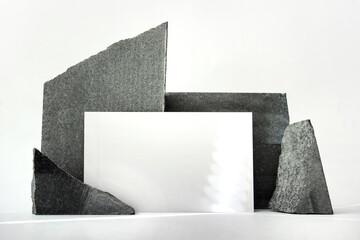 Mockup template with white horizontal card standing next to black natural raw stone on white backgorund. 