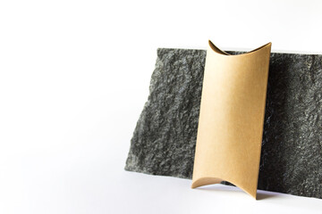 Mockup template with craft paper guft box standing next to raw natural black stone on white background. Image with copy blank space.