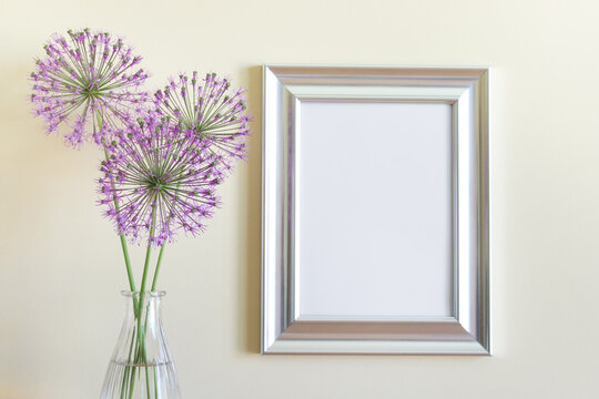 Mockup template with blank silver frame and purple summer garlic flowers next to yellow wall.