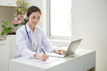 Young Female Doctor in white coat sitting at her workplace working. Doctor sitting at desk and writing a prescription for her patient. Smiling female doctor working in doctor’s office.
