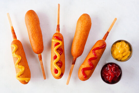 Corn dogs with a variety of toppings. Above view over a white marble background.