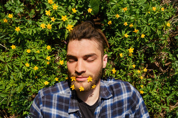 Spring flowers, close up portrait of man. Young Caucasian hipster with dreadlocks and flowers in...