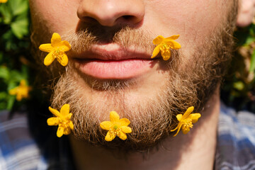 Spring flowers, close up portrait of man. Young Caucasian hipster with flowers in beard lies in...