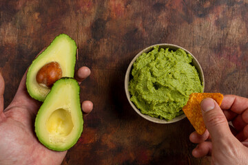 Traditional latinamerican mexican sauce guacamole in clay bowl, cut half avocado and avocado sandwiches on dark background. Top view