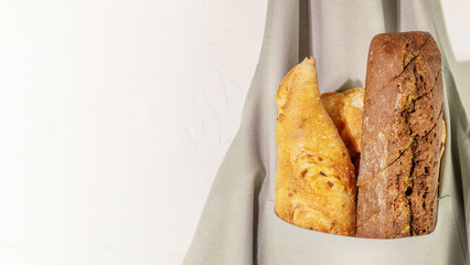 Different kind of natural bread. Eco friendly food composition with hande made fresh three loaf of bread in the pocket of a chef's apron on a white background with copy space. Crunchy french baguettes