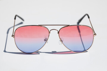 Sunglasses with pink and blue lenses on a white surface. Illuminated by strong sunlight. Vacation and well-being concept. - 504634091