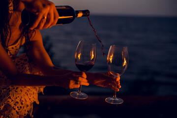 the process of filling a glass with red wine on the beach at sunset by the fire