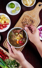 Soto indonesian traditional food on a bowl hold by male hand with spice and ingredients on the background