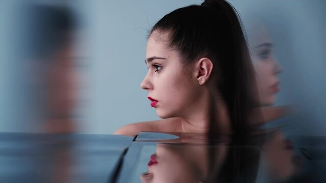 Beauty portrait. Facial treatment. Skin rejuvenation. Profile of pretty young woman face in blurred mirror glass reflection on blue background.