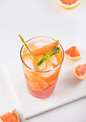 Fresh grapefruit juice with ice, mint and grapefruit slice in a glass on a white marble background with citrus  slices close up. Top view