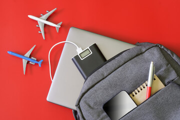 Gray backpack with gadgets: laptop, mobile phone, power bank, notepad and pen on red background...