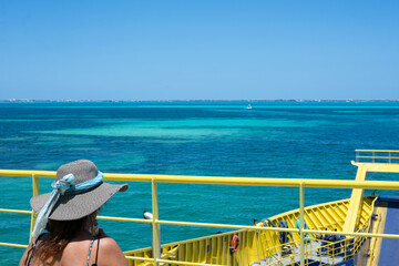 A woman in a sun hat observes the Caribbean Sea from a ferry ship in Mexico. Isla Mujeres.