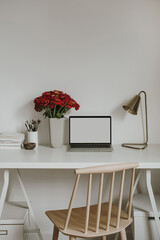 Laptop computer with blank screen on table with red gerber flowers bouquet. Aesthetic influencer styled workspace interior design template with mockup copy space