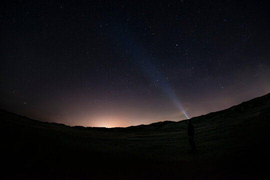 Adventurous man watching the stars on a beach at night with his headlamp shinning up at the stars.