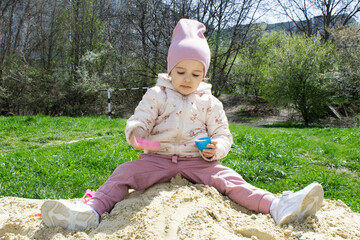 Little girl in the sandbox with shovels and a bucket on the playground. Child outdoors in summer. Summer fun. Summer sunny day in the sandbox.