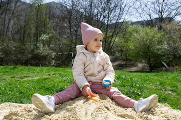 Little girl in the sandbox with shovels and a bucket on the playground. Child outdoors in summer....