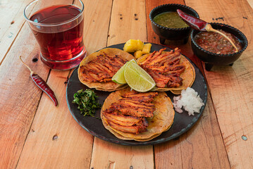 Tradicionales tacos mexicanos al pastor servidos en una mesa con salsas y agua fresca de jamaica