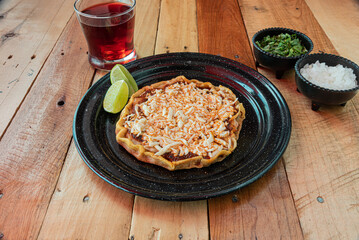 Tracional sope mexicano de queso servido en una mesa de madera con salsas y agua fresca de jamaica