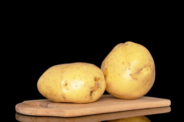 Two raw organic potatoes on a wooden cutting board, close-up, isolated on a black background.