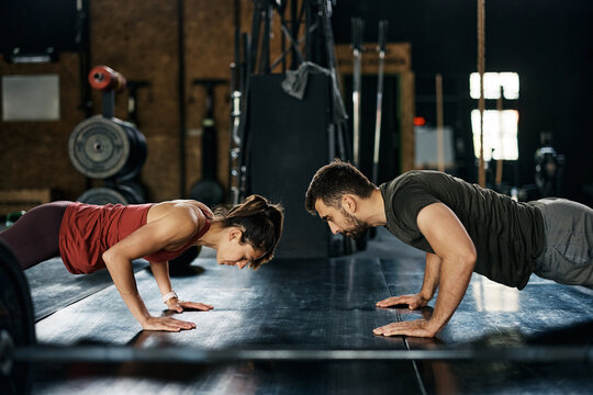 Athletic couple doing push-ups while having sports training in gym.