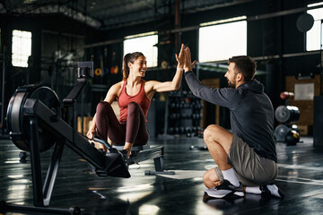 Fototapeta Happy athlete giving high-five to her personal trainer after exercising on rowing machine at gym. obraz