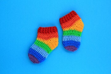 Rainbow handmade crochet baby socks booties on blue background. Baby shower greeting card, poster, banner top view concept