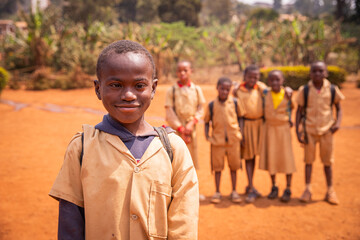 African schoolboy with Down syndrome in the schoolyard with his school mates out of focus in the background.