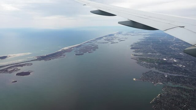 View from a window plane on Atlantic Ocean and coastal cities in the United States. Window aerial view from an airplane seat next to the wings