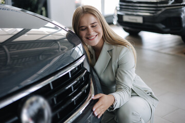 Business woman chossing a new car in a car showroom. Happy female hug new car and very glad....