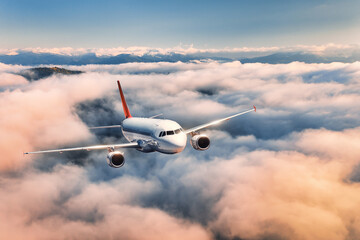 Airplane is flying above the clouds at sunset in summer. Landscape with passenger airplane,...