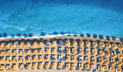 Aerial view of blue sea, empty sandy beach with sun beds and umbrellas at sunrise in summer. Blue lagoon in Oludeniz, Turkey. Tropical landscape with turquoise water, deck chairs. Travel. Top view