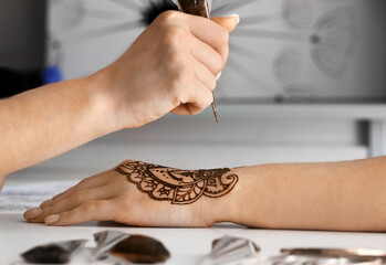 Mehndi master drawing henna tattoo on female hand in salon