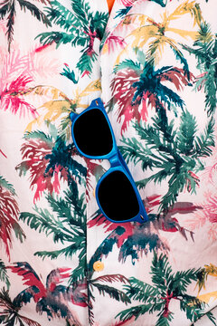 Close-up of blue sunglasses hanging from the Hawaiian shirt. 