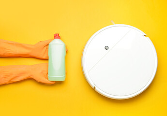 Female hands in rubber gloves, bottle of detergent and robot vacuum cleaner on color background